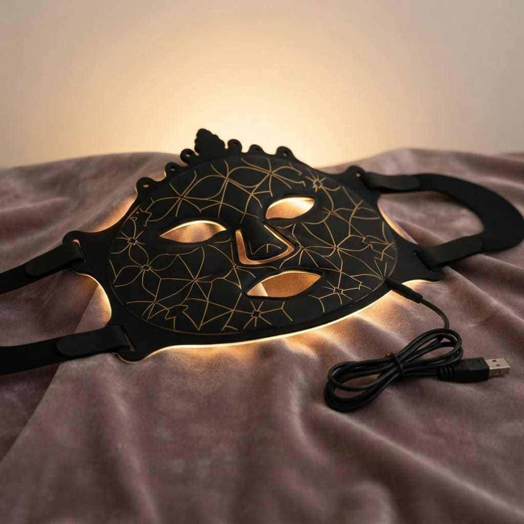 Pro Light Thera™ Mask, black flexible silicone with gold geometric line pattern, eye and mouth openings, and adjustable straps.